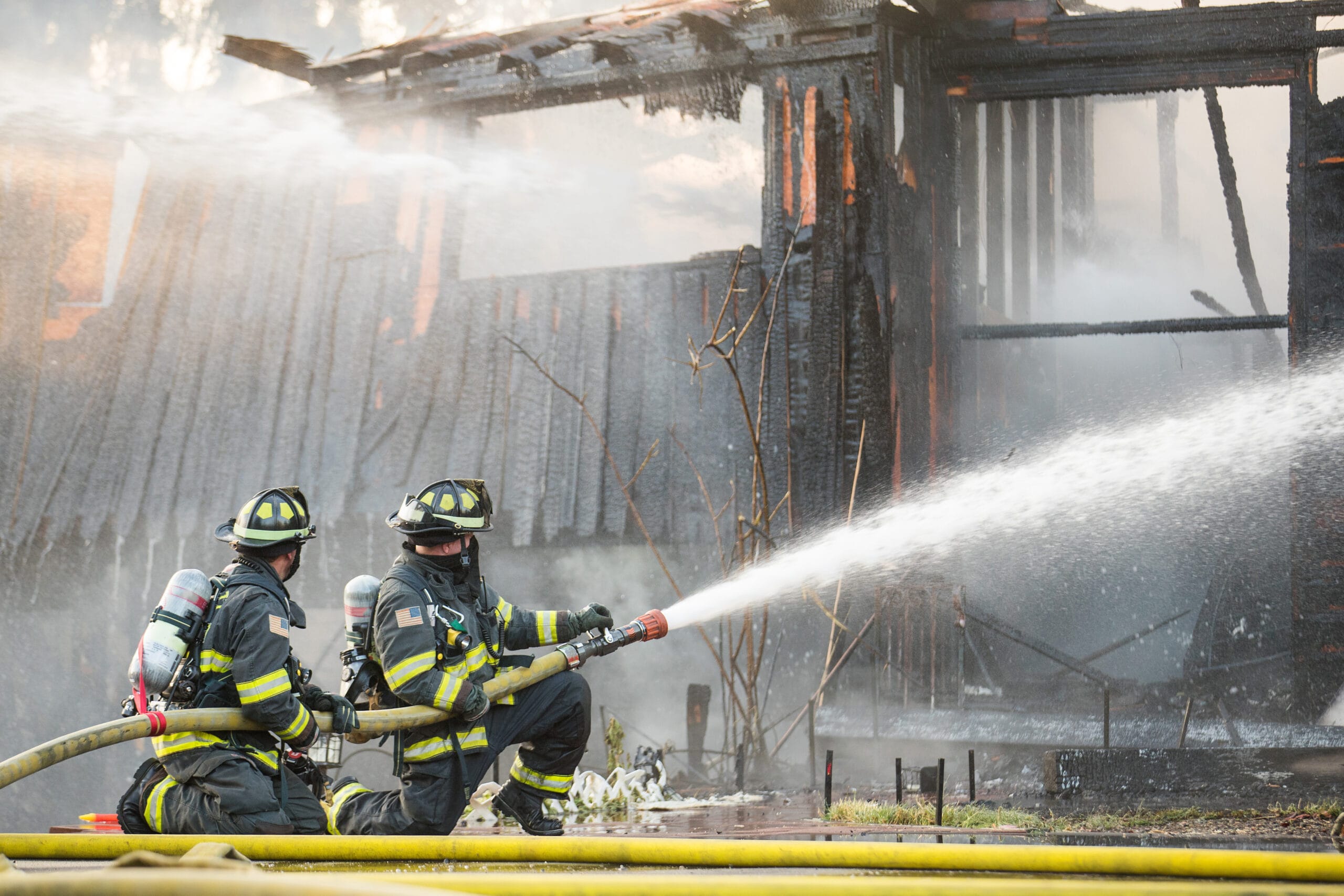 A residential home burns in a house fire as firefighters spay water from a hose in an effort to put it out.